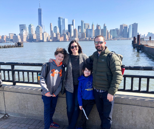 Brenna Schneider on a pier with family, water and New York City skyline in the background