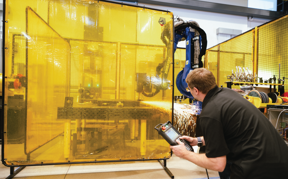 Photo of a man working with a robotic arm behind a yellow shield. 