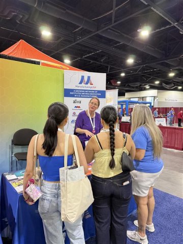 Photo of a group of three girls visiting Manufacturing USA's booth at the SkillsUSA conference talking to a network representative