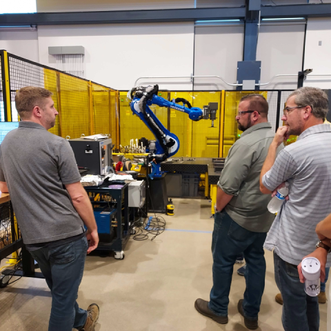 Photo of three men looking at a robotic arm