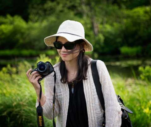 Photo of Ruby Gu in a white hat and sunglasses holding a camera outside