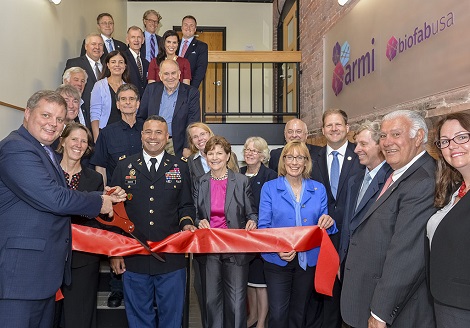 Photograph of members of the Board of Directors and Stakeholders Council for BioFabUSA holding and cutting a large red ribbon.