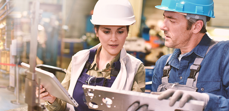 Photo of a man and woman inspecting a manufactured part and comparing it to digital information about the part on a tablet computer.